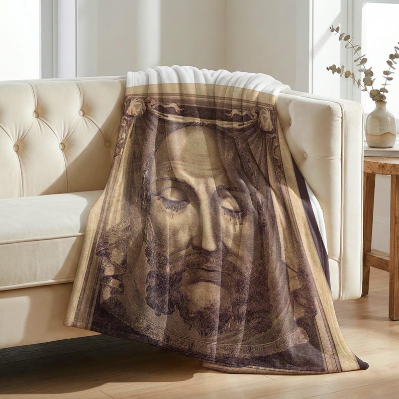 Holy Face plush blanket draped over the arm of a tufted cream sofa