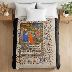 Plush blanket featuring a medieval illuminated manuscript page depicting the Nativity scene with ornate decorative borders and floral patterns, displayed on a bed with white pillows