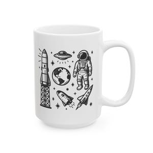 May include: White ceramic mug with a black and white illustration of an astronaut, a rocket, a spaceship, a UFO, and the Earth. The illustration is surrounded by stars.