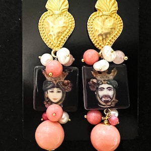 Könnte beinhalten: Goldene herzförmige Ohrringe mit einem Schwarzweißbild eines Männer- und Frauen Gesichts, rosa und weißen Perlen und einer goldenen Krone.