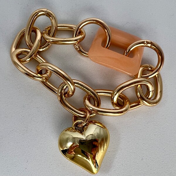 Bracelet doré avec pendentif coeur. Gros maillons en métal et un maillon en résine rose. Cadeau romantique et unisexe pour les amoureux.