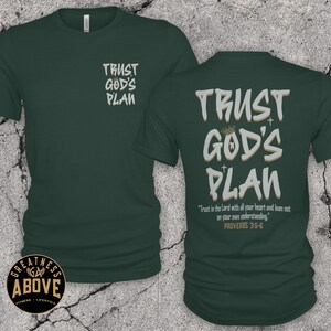 May include: A dark green short-sleeve t-shirt featuring the text "TRUST GOD'S PLAN" in white and tan on the front left chest and a larger version on the back, which also includes the text "Trust in the Lord with all your heart and lean not on your own understanding. PROVERBS 3:5-6."