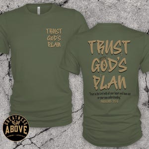 May include: An olive green short-sleeve t-shirt featuring the text "TRUST GOD'S PLAN" in tan on the front left chest. The back displays the same text in a larger font, along with the verse "Trust in the Lord with all your heart and lean not on your own understanding. PROVERBS 3:5-6."