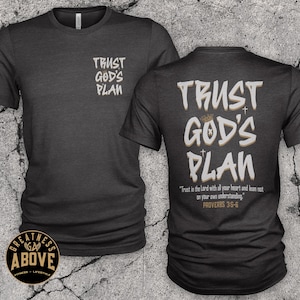 May include: A charcoal gray short-sleeve t-shirt featuring the text TRUST GOD'S PLAN on the front left chest and a larger version on the back with the verse Trust in the Lord with all your heart and lean not on your own understanding. PROVERBS 3:5-6.