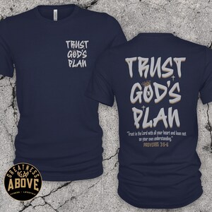 May include: A navy blue short-sleeve t-shirt featuring the text TRUST GOD'S PLAN on the front left chest. The back displays the same text in large letters with a crown and cross icons, plus the verse Trust in the Lord with all your heart and lean not on your own understanding. PROVERBS 3:5-6.