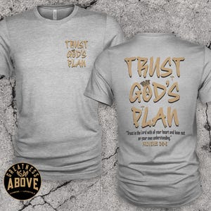 May include: A heather gray short-sleeve t-shirt featuring the text "TRUST GOD'S PLAN" in tan letters on the front left chest and a larger version on the back with a small crown icon, plus the verse "Trust in the Lord with all your heart and lean not on your own understanding. Proverbs 3:5-6."