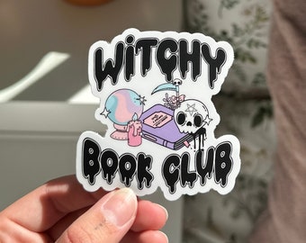 May include: A white sticker with black dripping lettering that reads "Witchy Book Club". The sticker features a cartoon illustration of a book, a skull, a crystal ball, a candle, and a scythe.