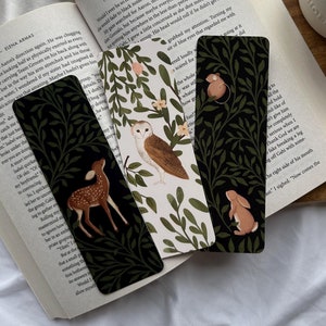 May include: Four bookmarks with black backgrounds and green vines. Each bookmark features a different animal: a deer, an owl, a rabbit, and a mouse. The bookmarks are on a book with the text "The Spanish Love Deception" visible.