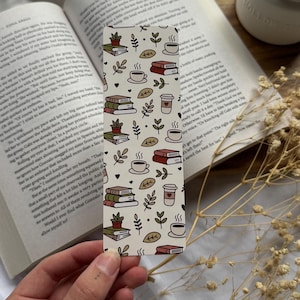 May include: A white bookmark with a repeating pattern of books, coffee cups, and leaves. The bookmark is decorated with a brown, green, and red colour scheme.
