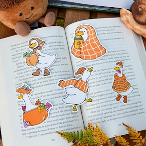 May include: A charming image with a plush acorn toy, an open book with duck stickers, and a snail figurine. The book shows butterfly illustrations. The duck stickers are wearing hats and scarves.