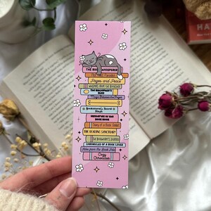 Peut inclure: Signet de lecture rose avec une pile de livres et un chat lisant "The Book Whisperer". Les titres des livres incluent "Post Paradise", "Pages and Peace", "Whispers from the Bookshop", "Magic Between the Pages", "Bookworm's Secret", "Mysteries of the Book Nook", "Diary of a Book Addict", "The Reading Sanctuary", "The Bookworm's Journal", "Chronicles of a Book Lover", "Tales from the Book Pile", "Cozy Chronicles".