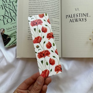 May include: A close-up of a book with a bookmark featuring a floral pattern of red poppies on a white background. The book is open to a page with the title "Palestine, Always".