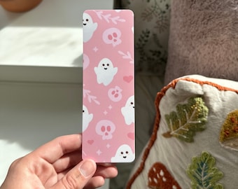 May include: Pink bookmark with a repeating pattern of white ghosts, skulls, and hearts.