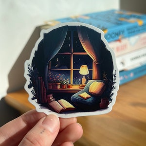 May include: A sticker featuring a cozy reading nook scene. The illustration depicts a window with a night sky view, a lit lamp, a comfortable armchair, and open books. The color palette includes blues, yellows, and greens.