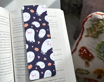 May include: A bookmark featuring a cute Halloween design with white ghosts, candy corn, pumpkins, and hearts on a dark blue background.