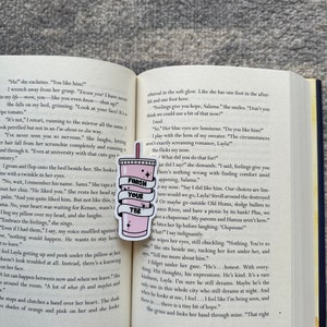 K&ouml;nnte beinhalten: Nahaufnahme eines rosa und wei&szlig;en Buches mit den Worten "Finish Your TBR" auf einem rosa Lesezeichen. Das Buch ist auf einer Seite mit Text &uuml;ber die Gef&uuml;hle einer jungen Frau f&uuml;r einen Mann aufgeschlagen. Der Text lautet: "Feelings give you hope, Salama."