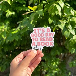 May include: Pink sticker with the text "It's a good day to read a book" and the word "spicy" written below in cursive.