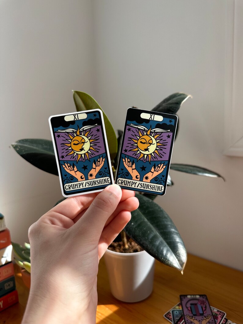 May include: Two stickers featuring a sun and moon with a face, a book, and hands. The stickers are on a white background with the text "XI GRUMPY/SUNSHINE".