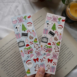 Könnte beinhalten: Zwei Lesezeichen zum Thema Weihnachten mit festlichen Illustrationen. Jedes Lesezeichen hat einen hellblauen Hintergrund mit Snoopy, dem Weihnachtsmann, Lebkuchenmännern und anderen Feiertags-Symbolen. Der Text "OH FUDGE" ist auf einem Fernseher zu sehen.