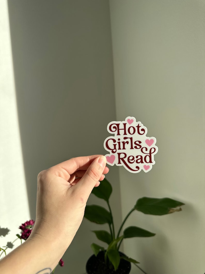 May include: A white sticker with the text "Hot Girls Read" in maroon lettering and pink hearts.