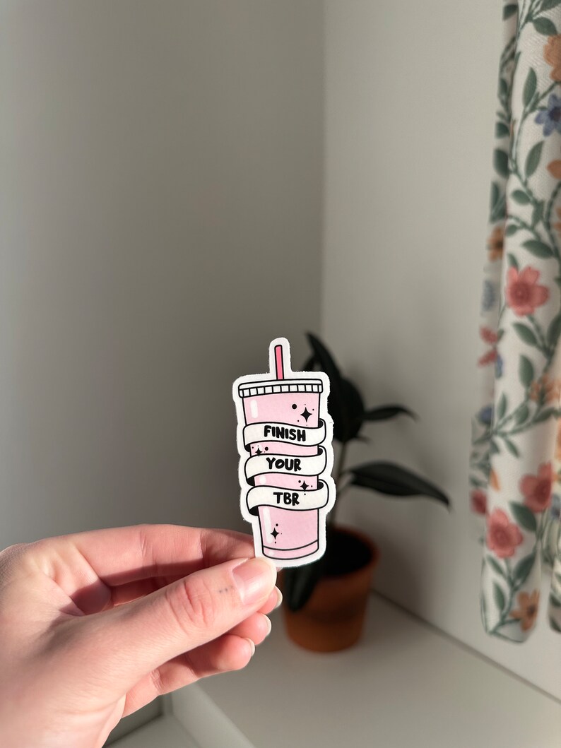 K&ouml;nnte beinhalten: Rosafarbener Aufkleber mit einem rosa Getr&auml;nk und dem Text "Finish Your TBR" in Schwarz.