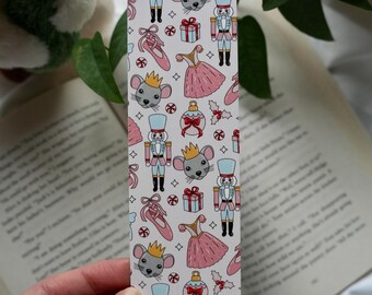 May include: A rectangular bookmark with a white background and a repeating pattern of ballet-themed illustrations. The design includes nutcrackers, mice, ballet slippers, dresses, and gift boxes in pink, blue, and red.