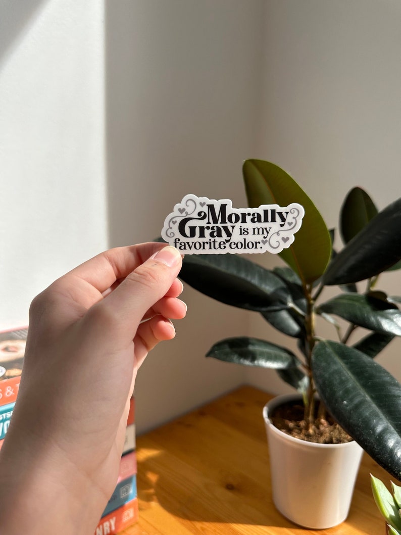 May include: A white sticker with black text that reads "Morally Gray is my favorite color." The sticker has a decorative swirl design and small hearts.