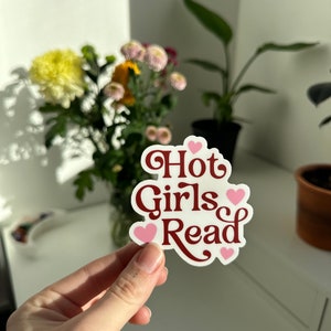 May include: White sticker with the text "Hot Girls Read" in red cursive font. The text is surrounded by four pink hearts.