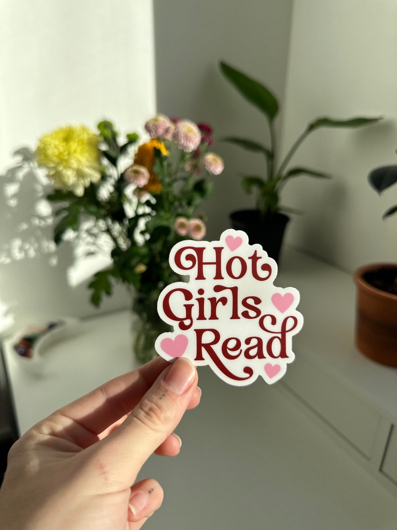 May include: White sticker with the text "Hot Girls Read" in red cursive font. The text is surrounded by four pink hearts.