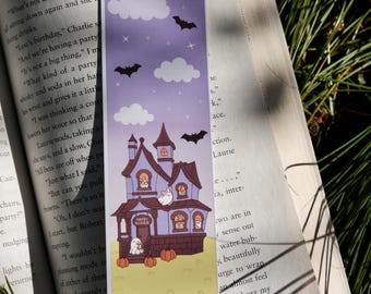 May include: A Halloween-themed bookmark featuring a purple house with ghosts, pumpkins, and bats. The bookmark has a purple sky background with white clouds and stars. The house has a sign that reads "Boo Books".