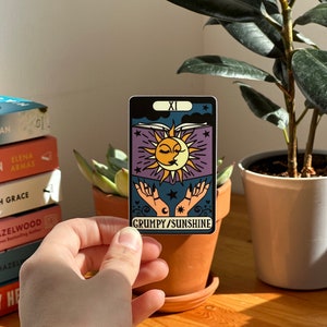 May include: A tarot card with a purple background and a sun and moon design. The card is labeled "XI GRUMPY/SUNSHINE".