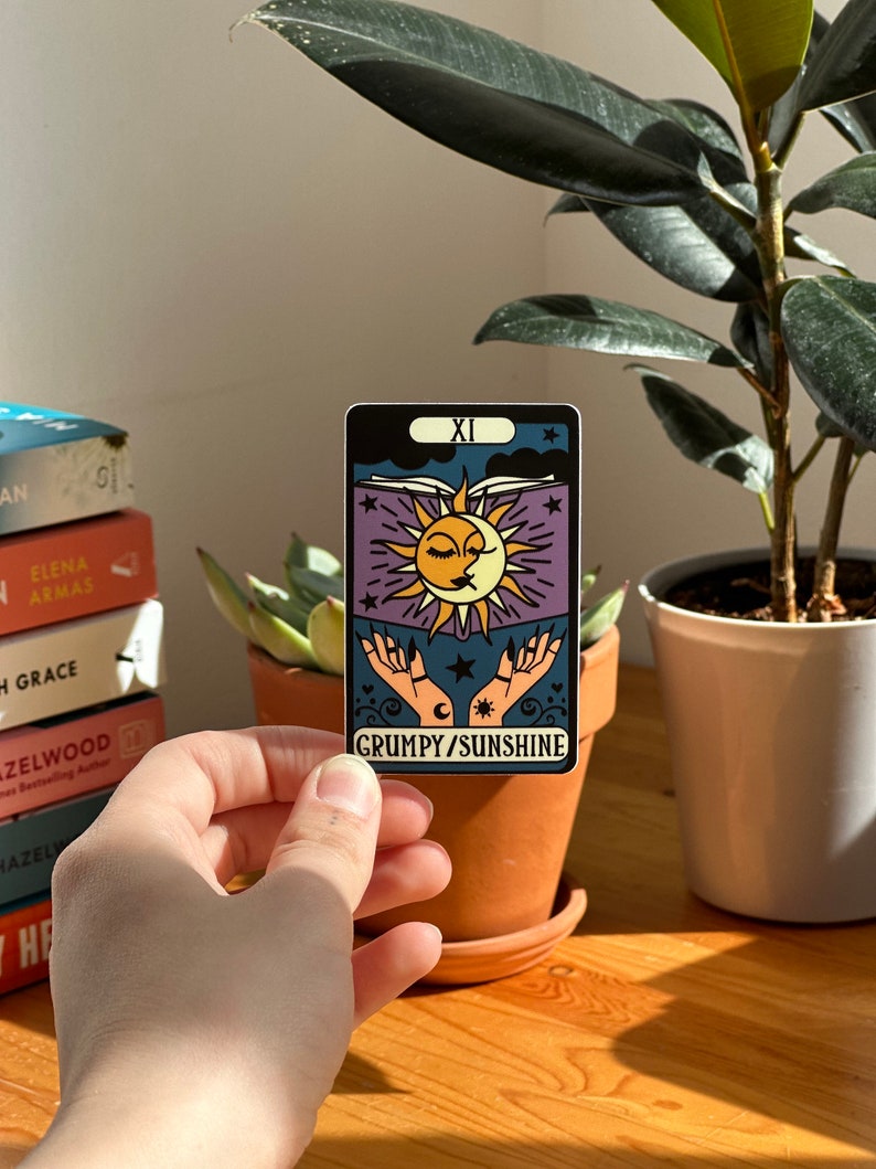 May include: A tarot card with a purple background and a sun and moon design. The card is labeled "XI GRUMPY/SUNSHINE".