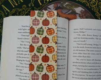 Puede incluir: Un marcapáginas decorativo con un diseño de calabazas naranjas, verdes y rosas sobre un fondo crema. El marcapáginas está colocado en un libro abierto titulado "A Natural History of Fairies".