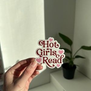 May include: A white sticker with the text "Hot Girls Read" in red cursive font. The sticker is decorated with pink hearts.