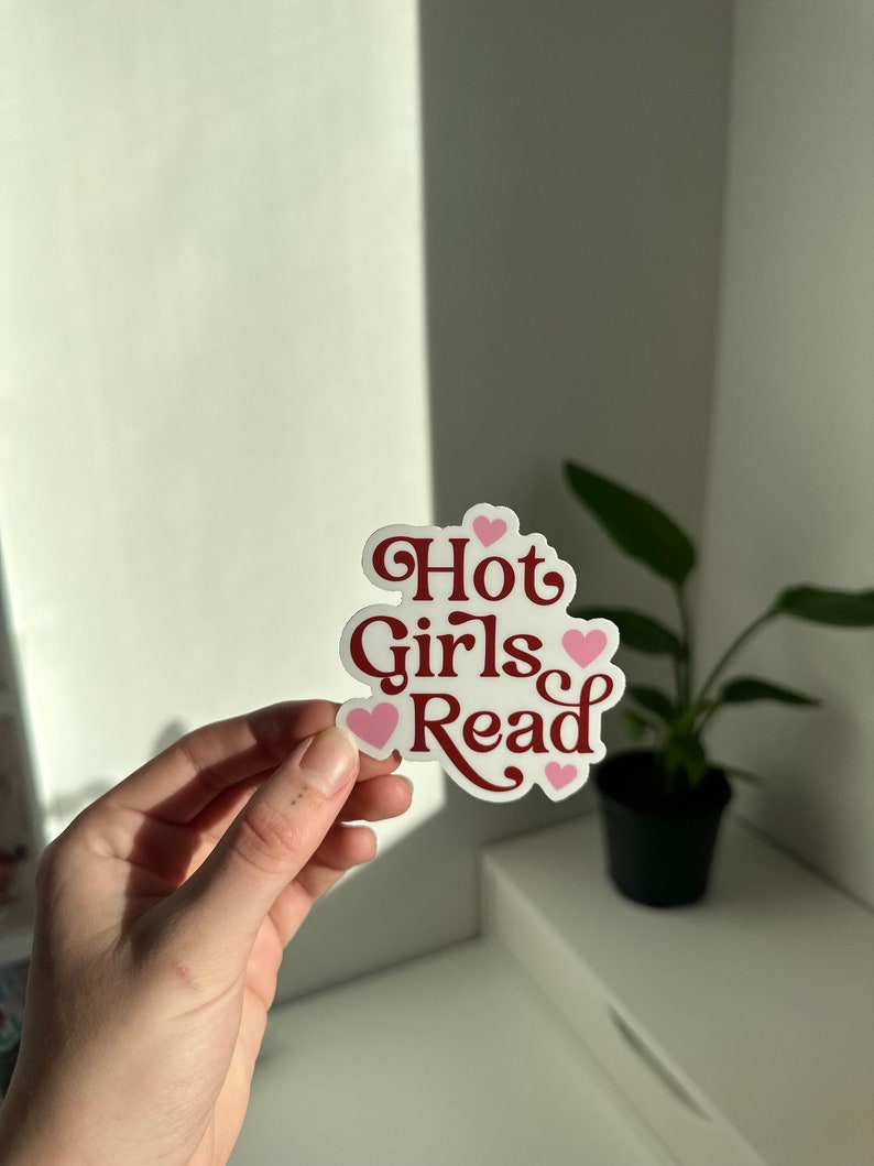 May include: A white sticker with the text "Hot Girls Read" in red cursive font. The sticker is decorated with pink hearts.