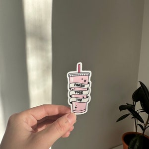 K&ouml;nnte beinhalten: Rosafarbener Aufkleber mit einer Cartoon-Illustration eines rosa Getr&auml;nks mit einem Strohhalm und dem Text "Finish Your TBR", der darum gewickelt ist.