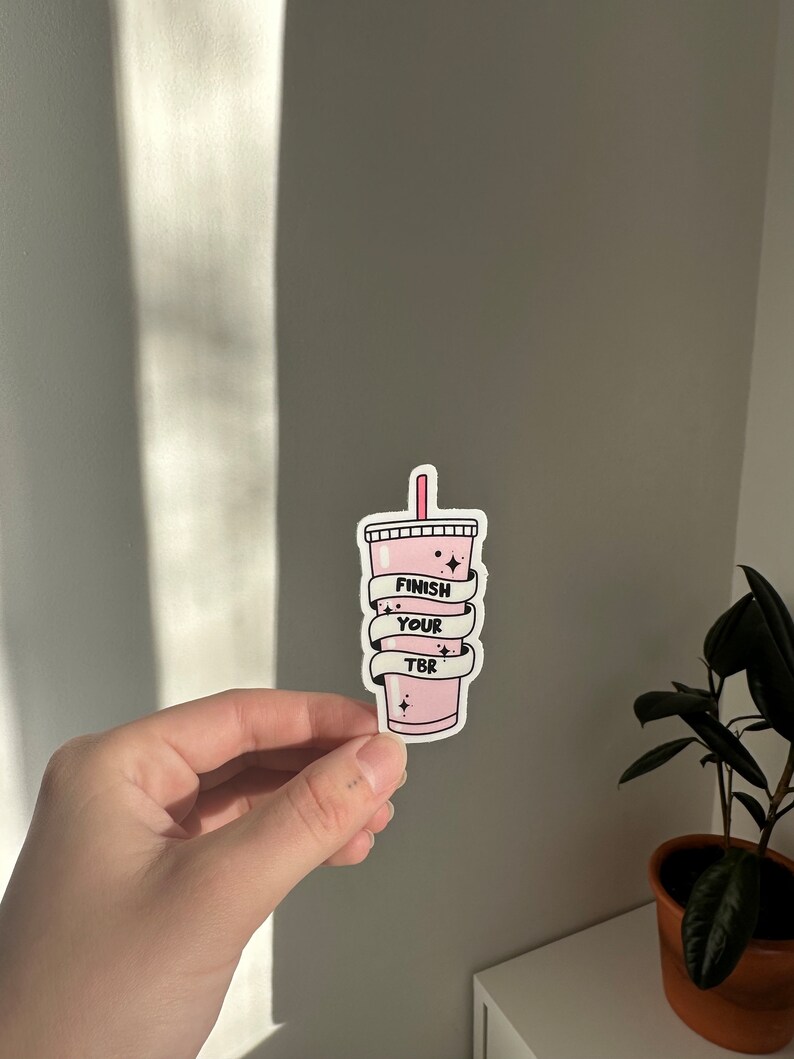 K&ouml;nnte beinhalten: Rosafarbener Aufkleber mit einer Cartoon-Illustration eines rosa Getr&auml;nks mit einem Strohhalm und dem Text "Finish Your TBR", der darum gewickelt ist.