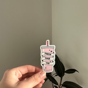 K&ouml;nnte beinhalten: Rosafarbener Aufkleber mit einem rosa und wei&szlig;en Becher mit Strohhalm und dem Text "Finish Your TBR" darauf.