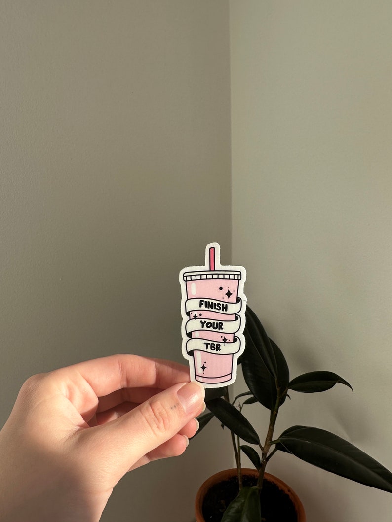 K&ouml;nnte beinhalten: Rosafarbener Aufkleber mit einem rosa und wei&szlig;en Becher mit Strohhalm und dem Text "Finish Your TBR" darauf.