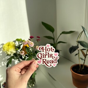 May include: A white sticker with the text "Hot Girls Read" in maroon letters and pink hearts around the text.