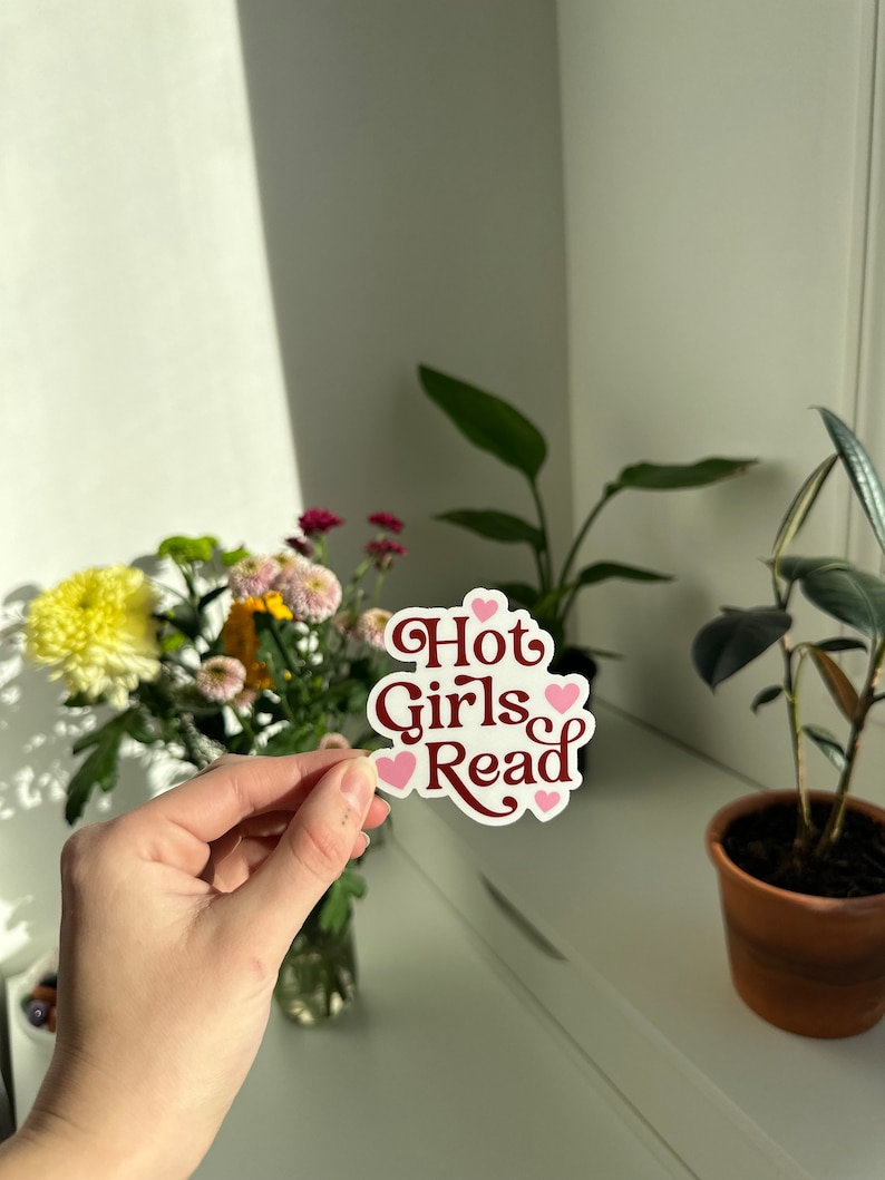 May include: A white sticker with the text "Hot Girls Read" in maroon letters and pink hearts around the text.