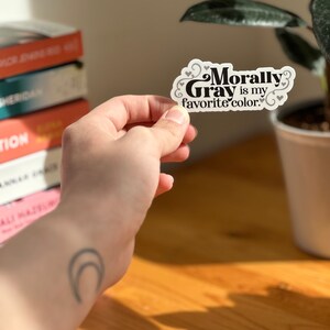 May include: A white sticker with black text that reads "Morally Gray is my favorite color." The sticker has small hearts around the text.