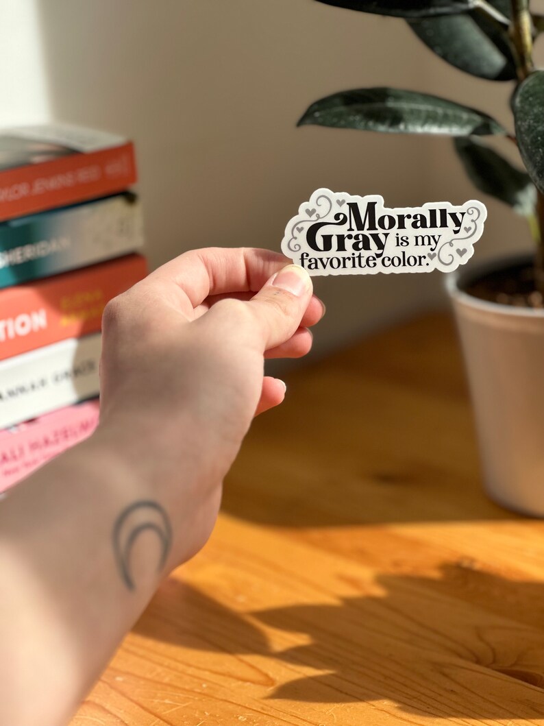May include: A white sticker with black text that reads "Morally Gray is my favorite color." The sticker has small hearts around the text.