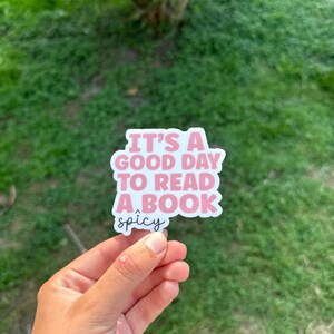 May include: A pink and white sticker with the text "It's a good day to read a book" and the word "spicy" underneath.