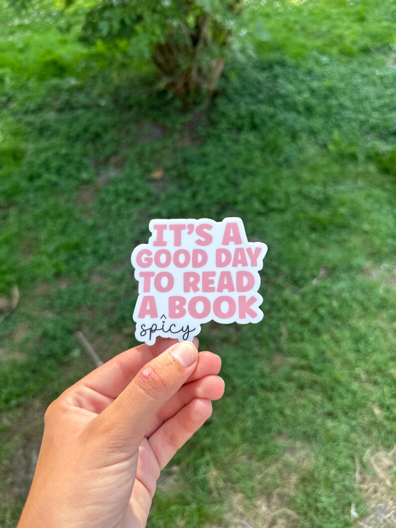 May include: A pink and white sticker with the text "It's a good day to read a book" and the word "spicy" underneath.