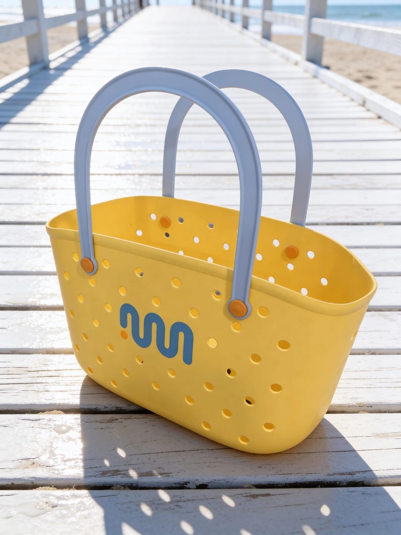 May include: A yellow tote bag with light blue handles and a blue wave-like logo. The bag has small circular perforations and orange accents. The bag is sitting on a white wooden surface.