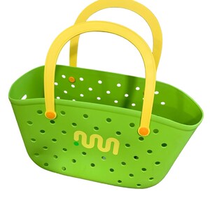 May include: A bright green tote bag with yellow handles. The bag has a perforated design and a yellow logo on the front. The handles are arched and attached with orange fasteners. The bag is designed for carrying items.