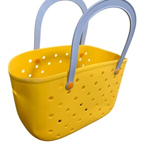 May include: A yellow tote bag with a perforated design. The bag has two gray handles and orange accents. The bag is made of a durable material and is designed for carrying items. The bag is a bright and cheerful color.