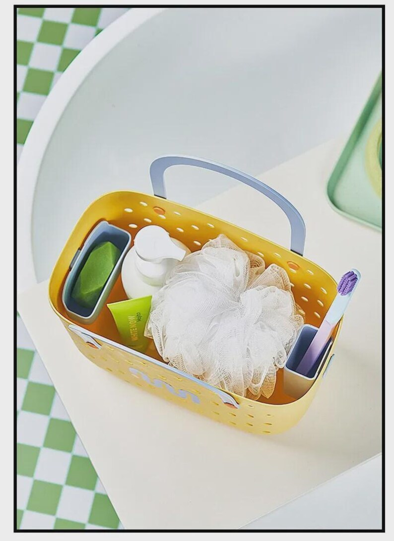 May include: A yellow rectangular caddy with a blue handle, holding toiletries. The caddy contains a green bar of soap, a white pump bottle, a loofah, a tube of toothpaste, and a toothbrush. The caddy is on a white surface.