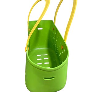 May include: A bright green plastic basket with yellow handles. The basket has a rectangular shape with a series of holes and slots for drainage. The handles are arched and attached to the top of the basket.